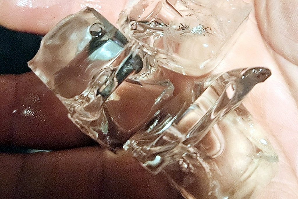 Hand holding thin hollow ice fragments that never formed into complete cubes, produced by a commercial ice machine with restricted airflow