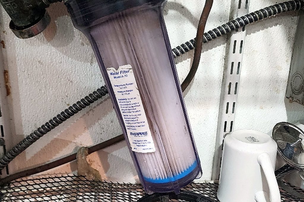Clear water filter housing plumbed into the ice machine supply line, the cartridge inside visibly discoloured
