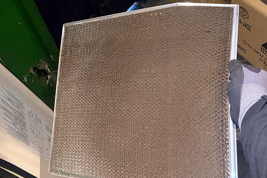 Metal mesh air filter pulled by hand from the front panel of an air-cooled commercial ice machine