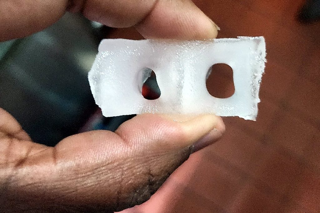 Hand holding a slab of ice that is completely opaque white through its whole thickness rather than clear