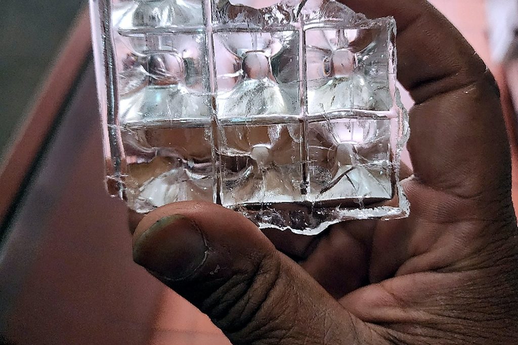 Hand holding a sheet of clear well formed ice cubes still joined together, produced after the water filter was replaced