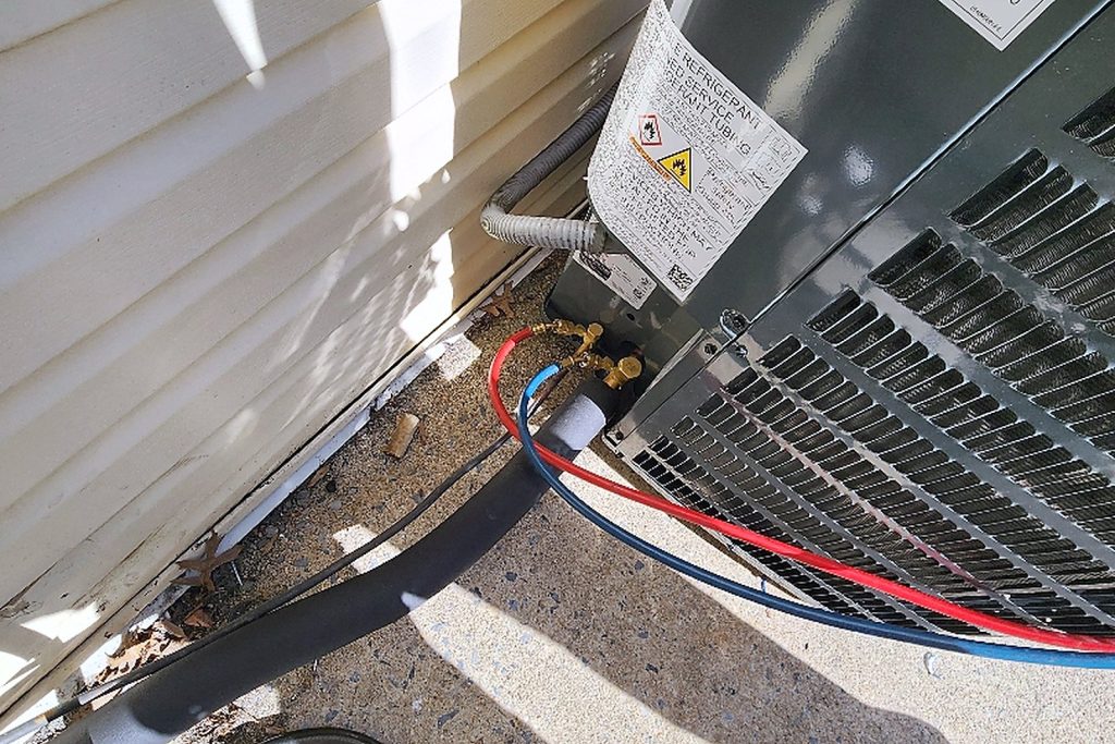 Refrigerant line set and electrical connections made up neatly at the base of an outdoor condensing unit