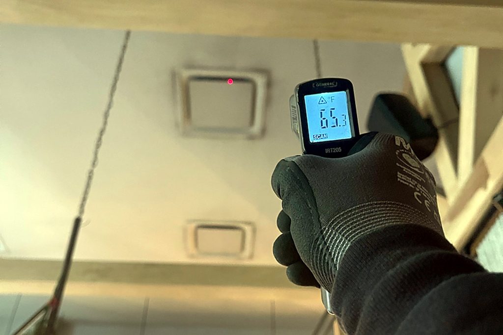 Infrared thermometer pointed at a ceiling supply register reading 65 degrees Fahrenheit