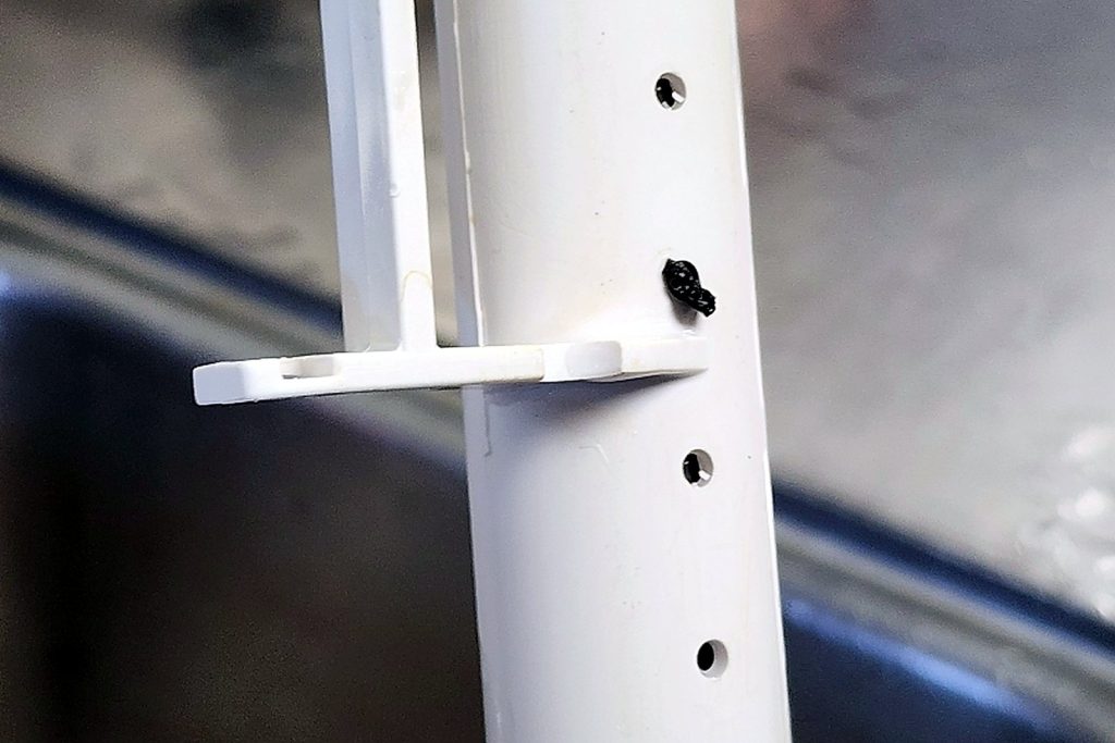 White plastic water distribution tube from an ice machine with its spray holes narrowed and stained by scale