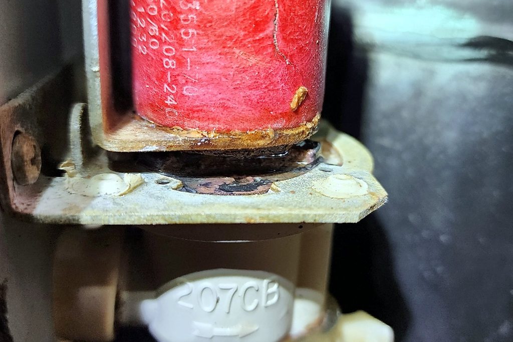 Red-coiled water inlet solenoid valve inside the ice machine with scale deposits around its base