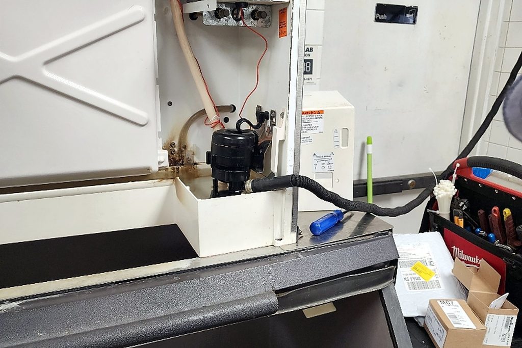 Ice machine with its front panel off and the bin door open during a cleaning service