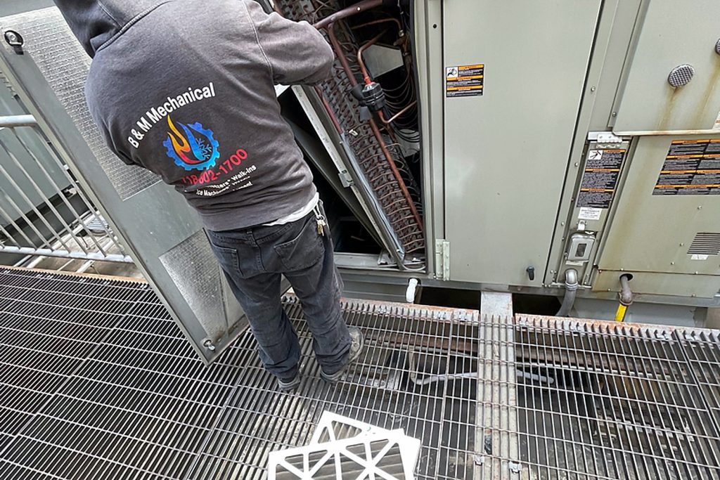 Technician seen from behind at the open filter section of a rooftop unit on a Manhattan roof