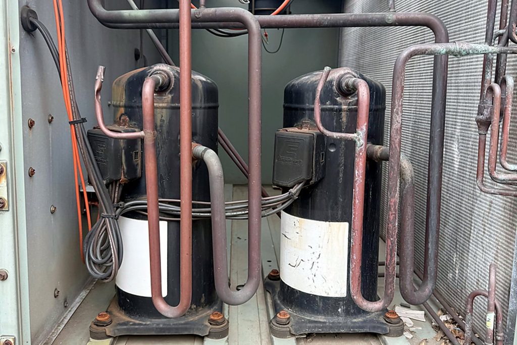 Compressor compartment of a rooftop unit showing two compressors with copper suction and discharge lines