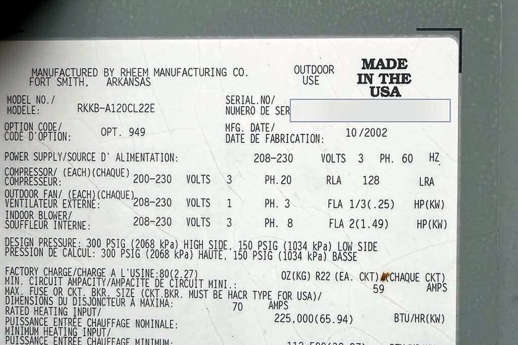 Data plate of a Rheem RKKB-A120CL22E rooftop unit listing R-22 refrigerant and a fabrication date of October 2002, with the serial number redacted