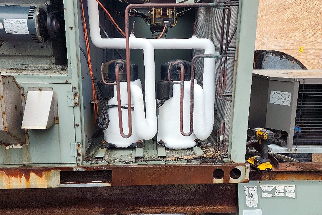 Open compressor section of a rooftop unit showing two compressors with insulated suction lines