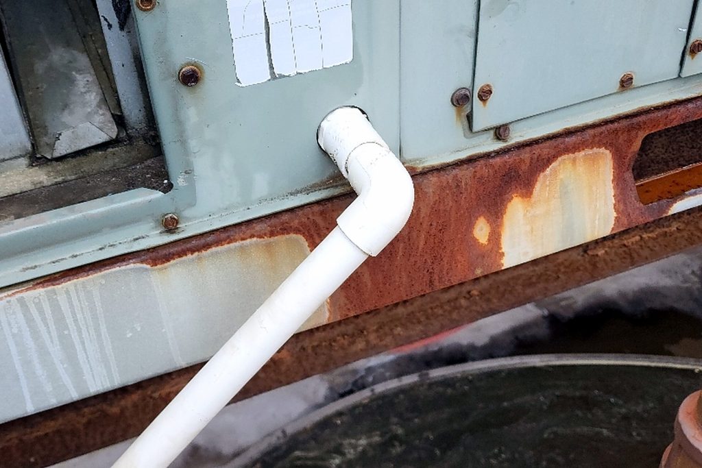 Exterior of a packaged rooftop unit with a white PVC condensate drain line running from it
