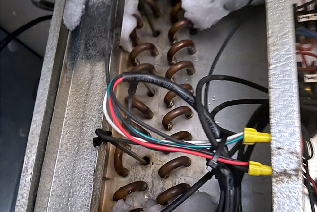 Close view inside the evaporator housing showing the coil, wiring and defrost heater elements encased in ice