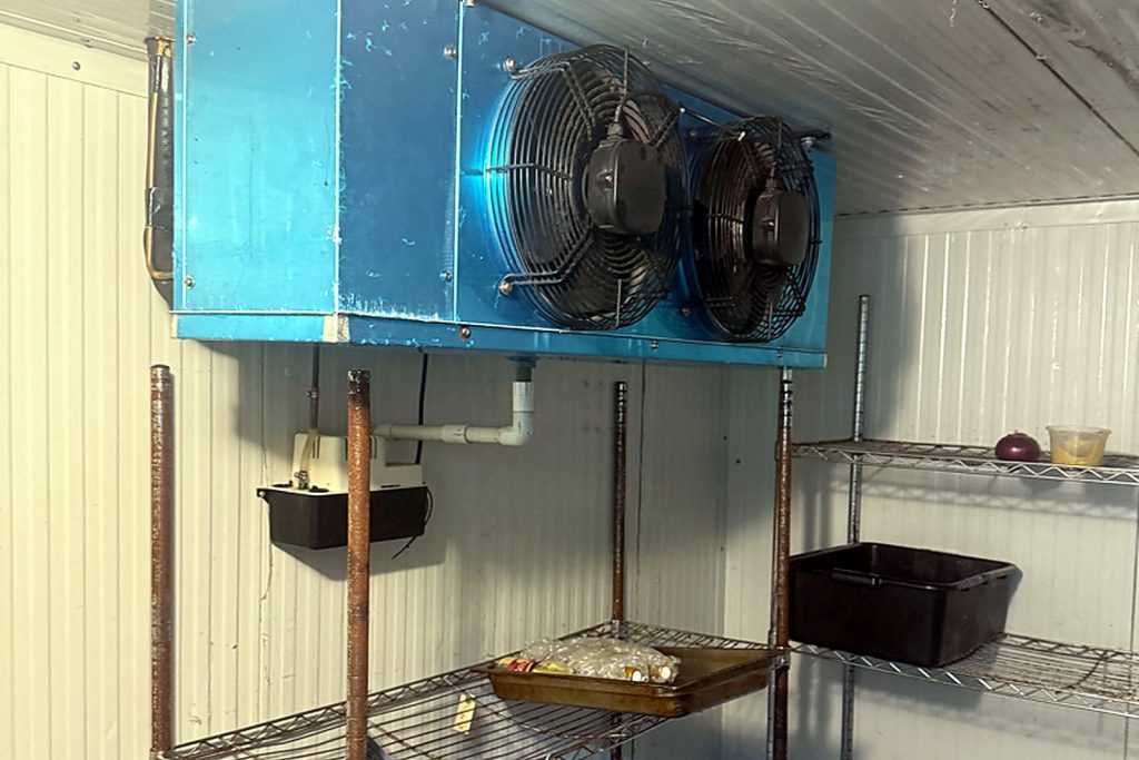 Two-fan evaporator mounted at the ceiling of a walk-in cooler above wire shelving